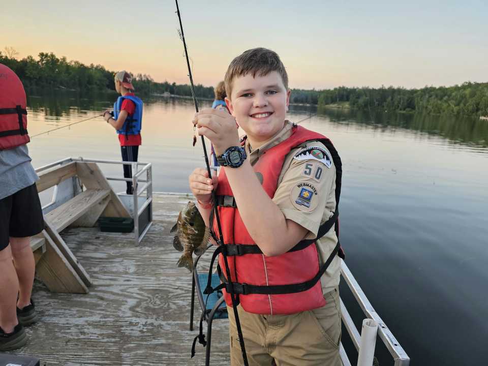 A boy smiles with his fishing pole inside a pontoon boat atop Lake Killian